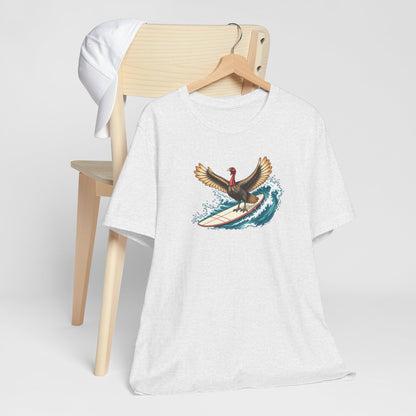 Ash gray surfing turkey Thanksgiving T-shirt featuring a teal wave and vintage-inspired island artwork hanging off a light wooden chair.
