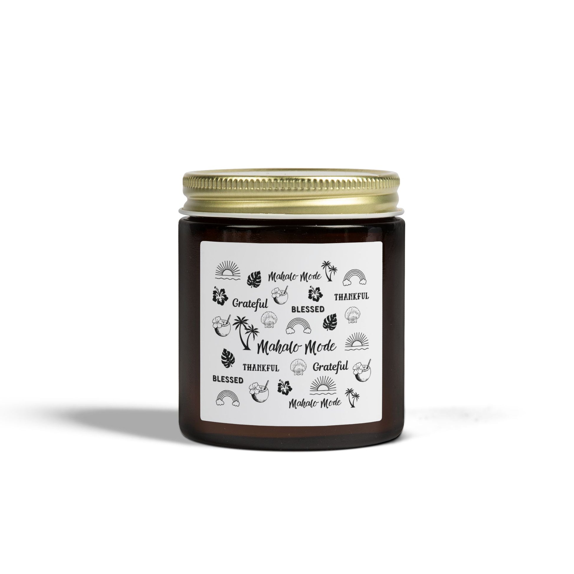 A dark amber glass jar candle with a gold metal screw-on lid and a white paper label featuring black hand-drawn style illustrations and the words 'Mahalo • Mode', 'Grateful', 'BLESSED', and 'THANKFUL'.
