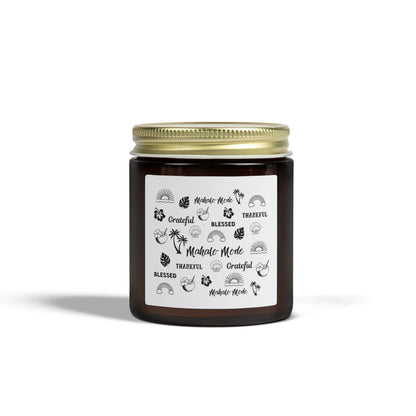A dark amber glass jar candle with a gold metal screw-on lid and a white paper label featuring black hand-drawn style illustrations and the words 'Mahalo • Mode', 'Grateful', 'BLESSED', and 'THANKFUL'.