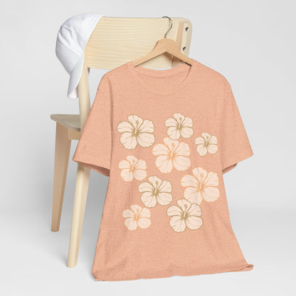 Peach Hibiscus All Over Graphic Tee featuring scattered tropical hibiscus flowers on a soft unisex tee inspired by island life in Hawaii hanging on a wood chair.