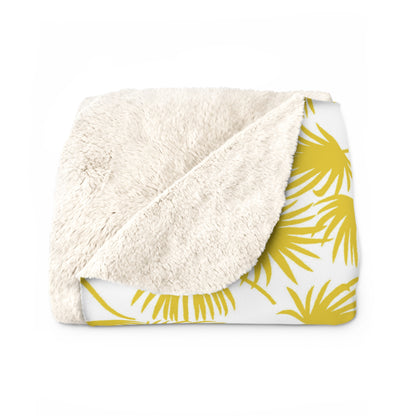 A folded throw blanket featuring a plush, cream sherpa fleece backside and a white front side printed with a yellow palm leaf pattern, shown on a plain white background.