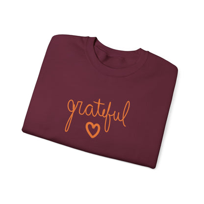 A folded burgundy crewneck sweatshirt featuring the word 'grateful' in orange cursive script and an orange heart outline on the front, set against a plain white background.