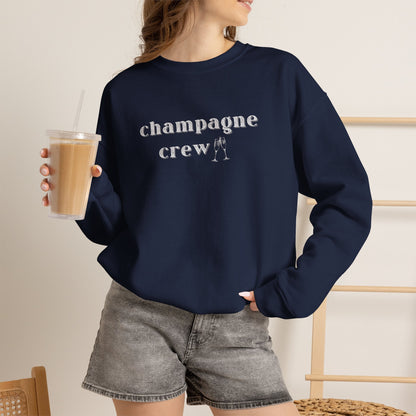 Woman wearing a navy graphic sweatshirt with text 'champagne crew' in white letters holding an iced coffee