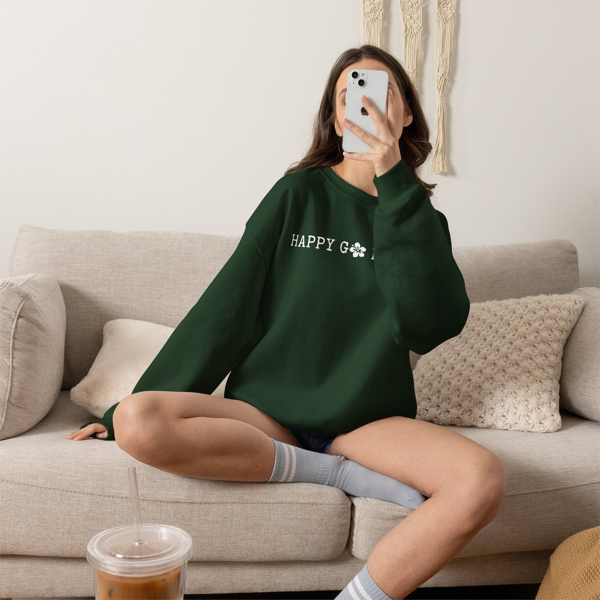 Person wearing a green sweatshirt with a graphic design ʻHAPPY GO LUCKYʻ, sitting on a couch in a living room.