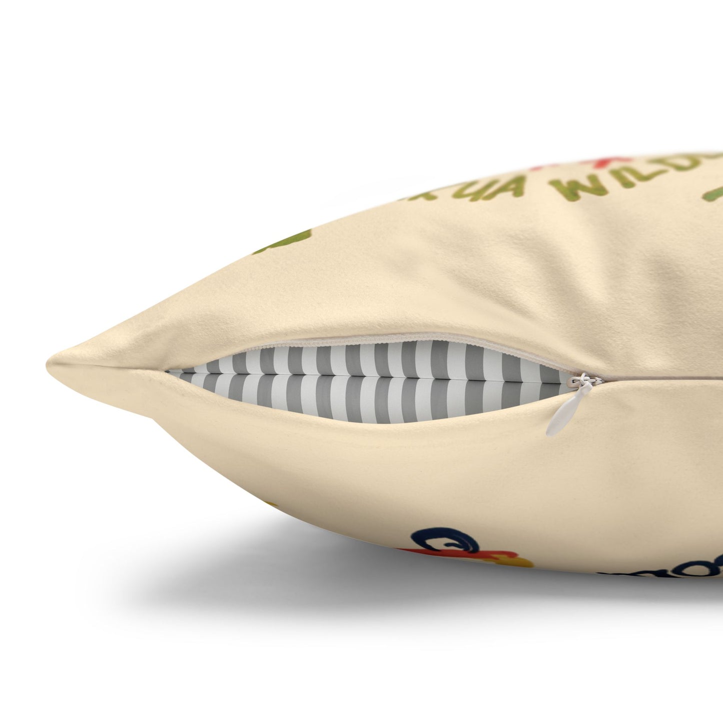 A close-up of a cream-colored throw pillow with a partially unzipped front, showing a gray and white striped inner cushion. The cream fabric has a colorful, partially visible graphic print.