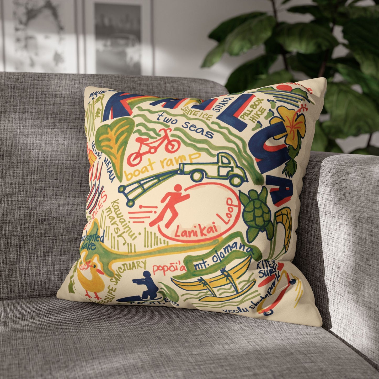 Decorative faux suede throw pillow cover featuring an original hand-drawn illustration of Kailua, Hawaii landmarks, beaches, surfing, paddling, turtles, and island icons sitting on a grey couch.