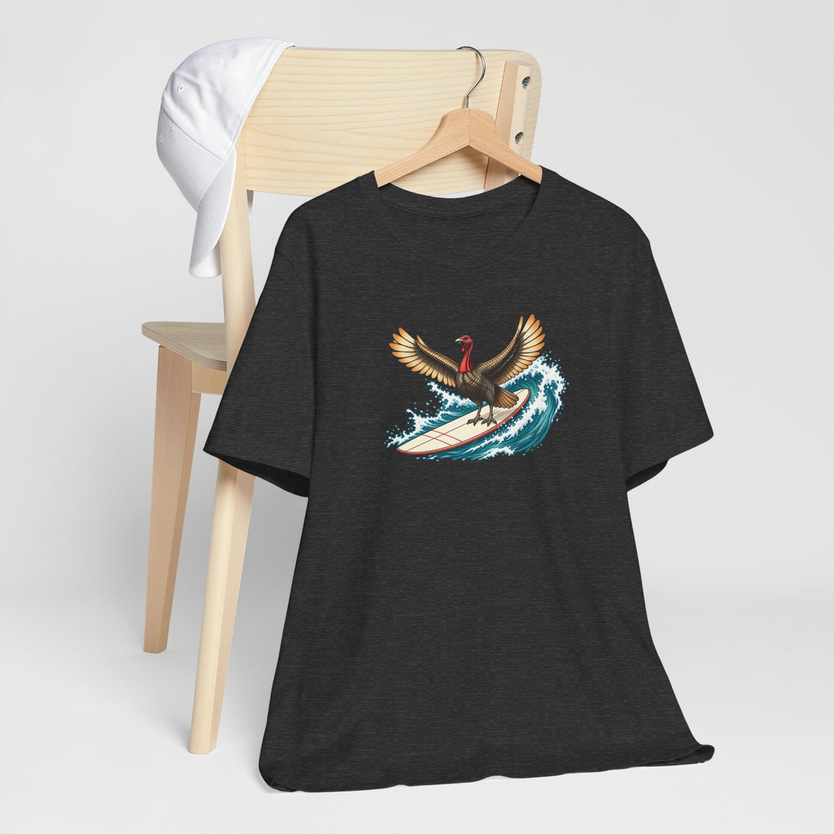 Dark gray surfing turkey Thanksgiving T-shirt featuring a teal wave and vintage-inspired island artwork hanging off a light wooden chair.