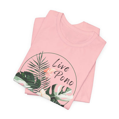 A folded light pink t-shirt with a tropical graphic print featuring palm leaves, a pink flower, and the text 'Live Pono' inside a thin circular outline, shown on a plain white background.