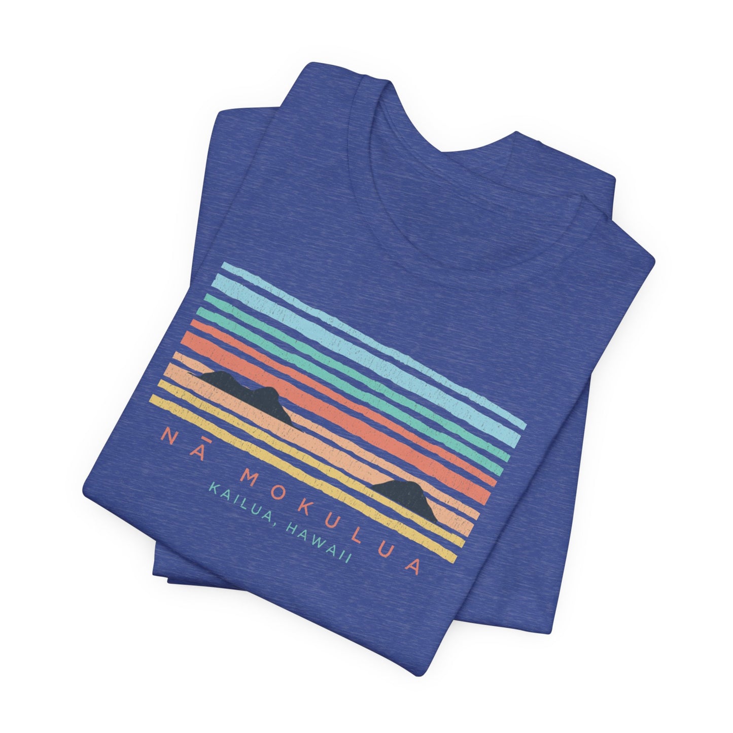 A folded heathered blue t-shirt featuring a retro sunset graphic with the text 'NÁ MOKULUA KAILUA, HAWAII'. The graphic contains horizontal stripes in shades of teal, light blue, orange, yellow, and pink, with two black mountain silhouettes.