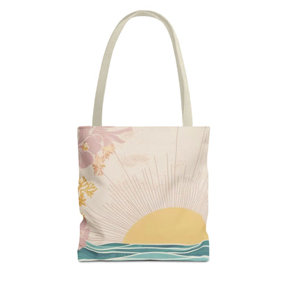 A canvas tote bag with a retro-style tropical sunset print, featuring a yellow sun, pink flowers, and teal ocean waves on a cream background, with light beige shoulder straps.
