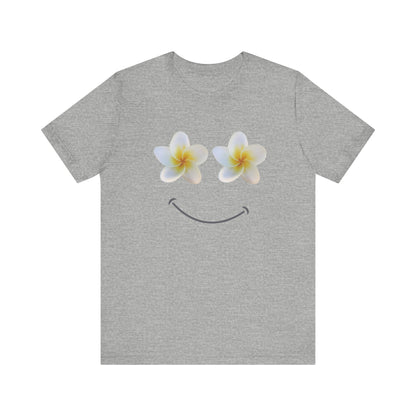A heather gray short-sleeve t-shirt with a graphic of two white plumeria flowers forming eyes and a curved smile on the chest, displayed against a solid white background.
