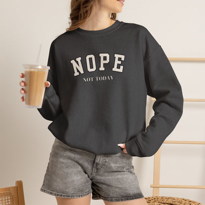 A woman wearing a dark charcoal gray crewneck sweatshirt with the text 'NOPE NOT TODAY' printed in white on the front, paired with gray denim shorts and holding an iced coffee.