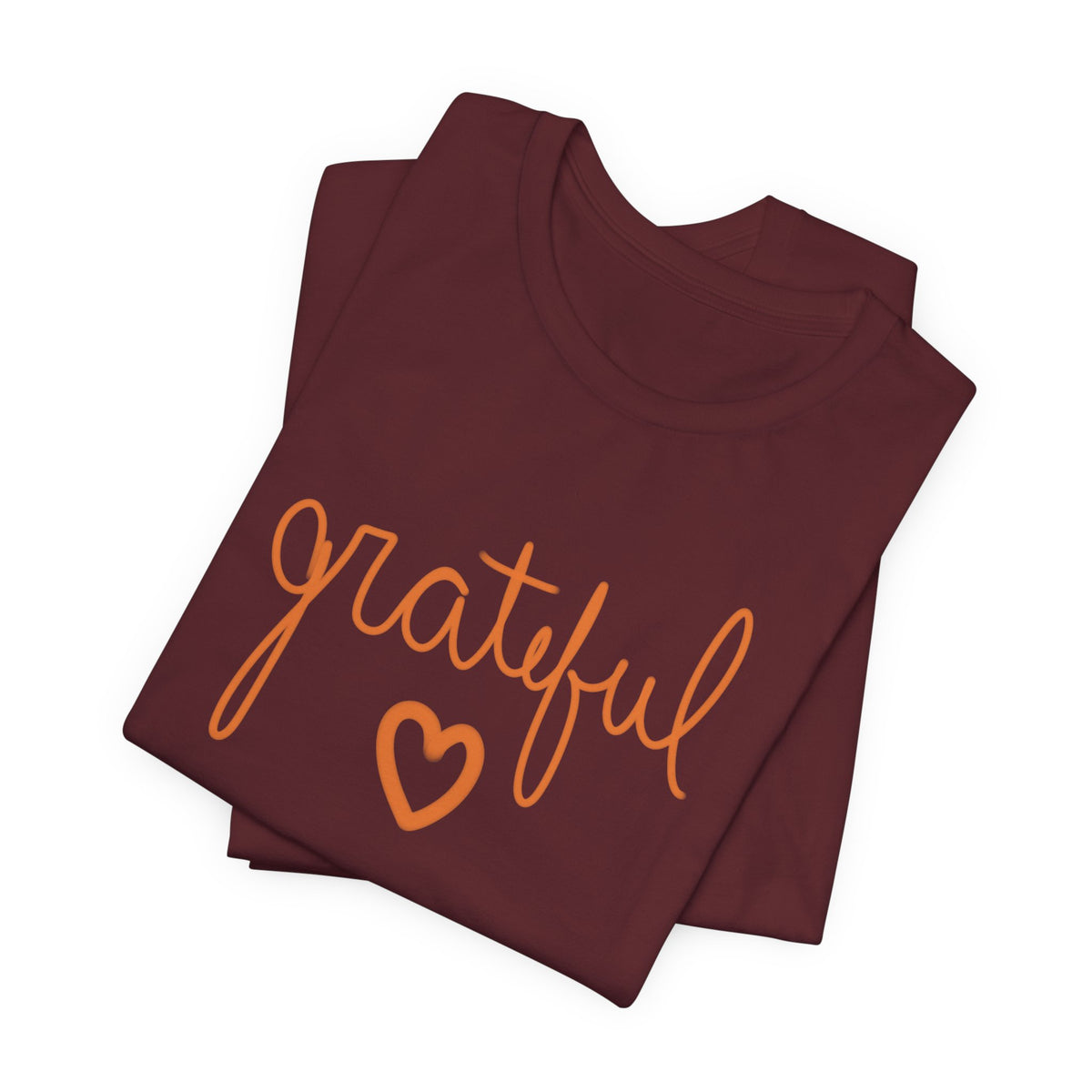 A folded burgundy t-shirt with the word 'grateful' written in orange cursive script and a matching orange heart underneath, displayed on a clean white background.