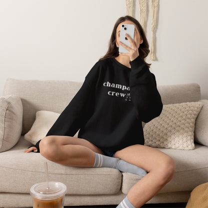 Person wearing a black sweatshirt with a graphic print 'champagne crew', sitting on a couch in a living room.