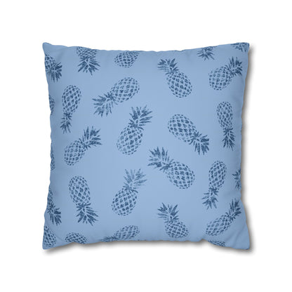 A square throw pillow featuring a repeating dark blue pineapple pattern on a light blue background, shown against a plain white studio backdrop.