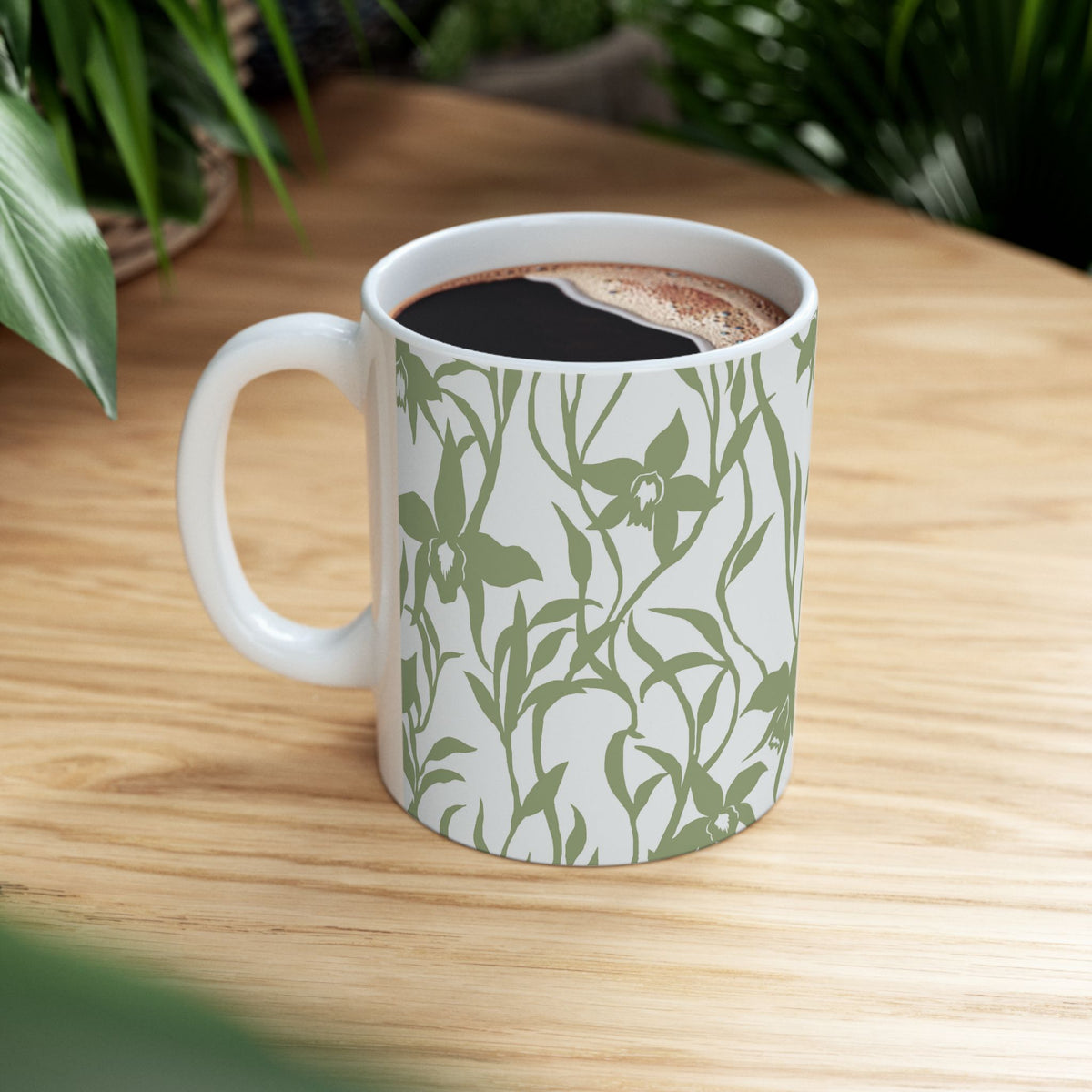Orchid Sage coffee mug with tropical orchid print by Global Village Kailua sitting on wood table with green plants.