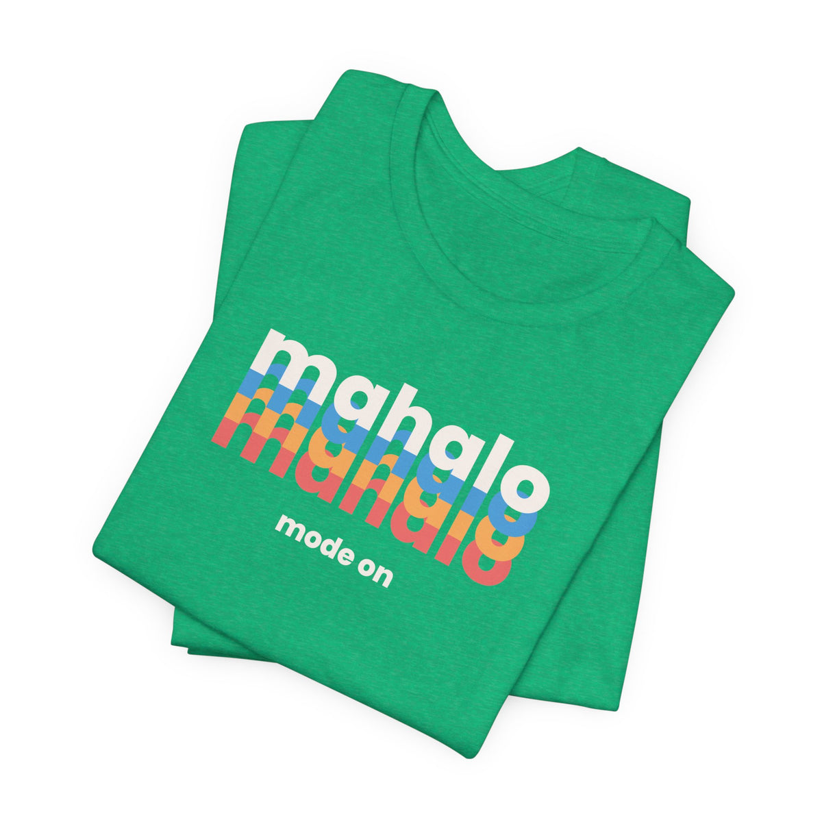 A folded green t-shirt with a colorful retro-style graphic reading 'mahalo mahalo' in white, blue, orange, and red, with 'mode on' printed below in white, shown on a plain white background.