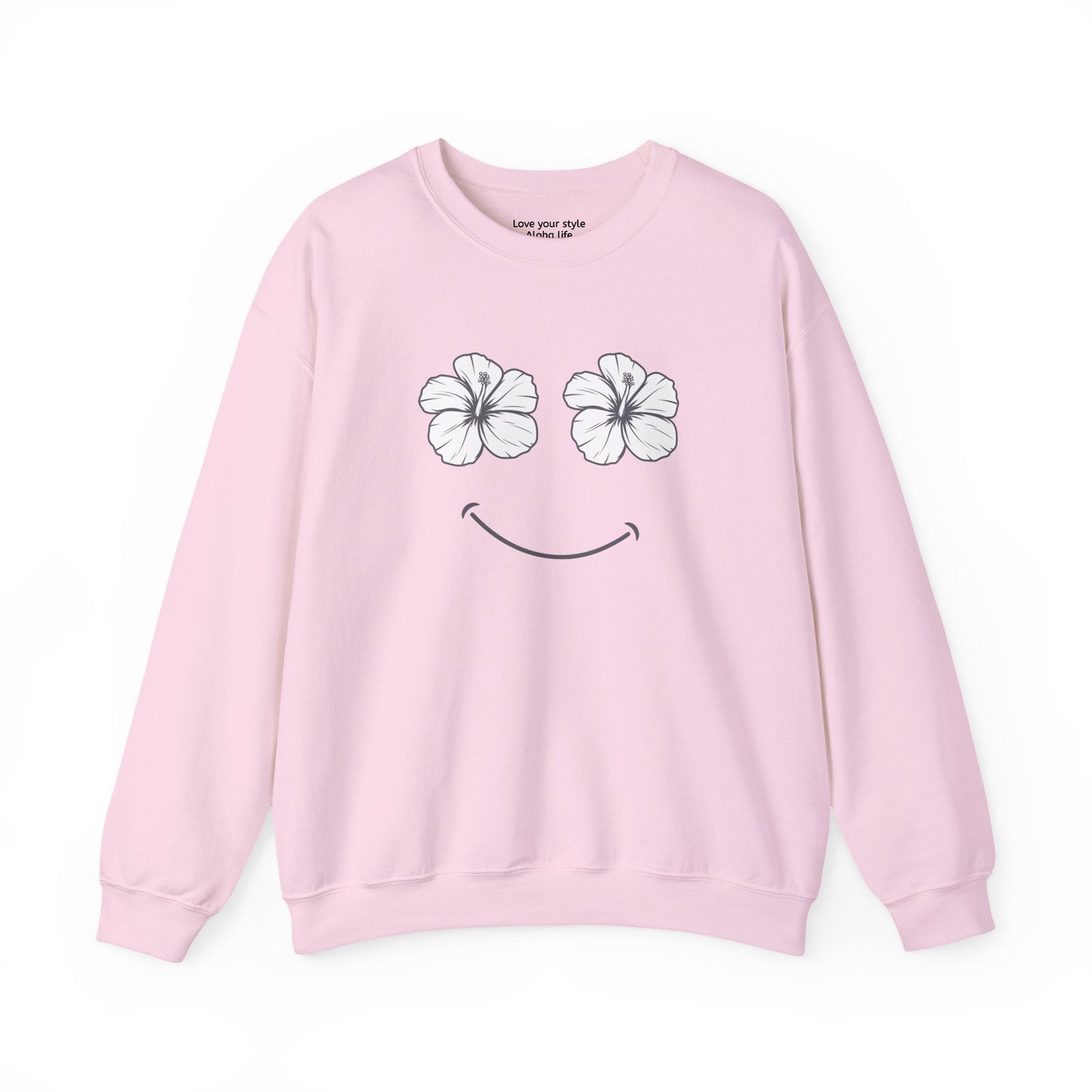 A light pink crewneck sweatshirt featuring a graphic of two white hibiscus flowers forming eyes and a simple black smiley curve below, displayed on a clean white background.