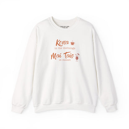 An white crewneck sweatshirt featuring a coral orange graphic print on the front that reads 'Kona in the mornings Mai Tais at sunset' with small illustrations of a coffee cup and a cocktail glass.