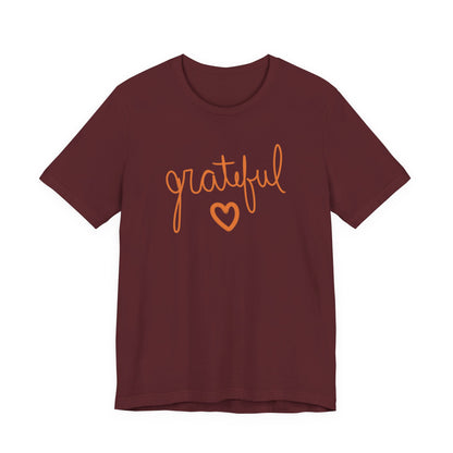 A short-sleeve crewneck t-shirt in maroon with the word 'grateful' written in orange cursive script and a matching orange heart underneath, shown on a plain white background.