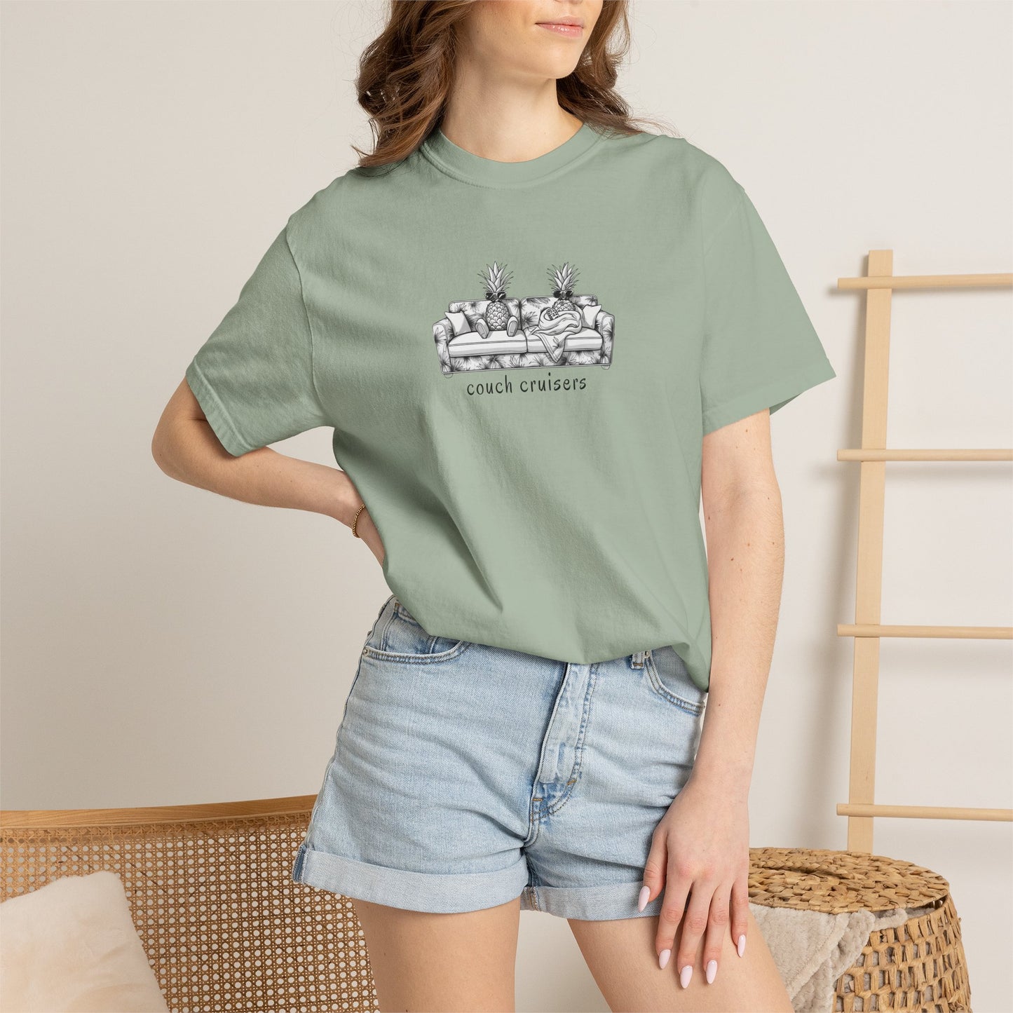 Person wearing a green couch cruisers comfort colors t-shirt with text and graphics, standing against a neutral background.