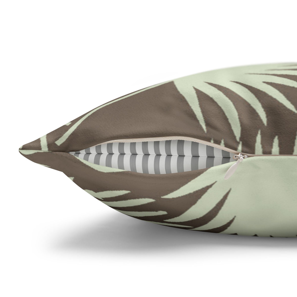 A close-up of a decorative throw pillow with a brown and pale sage green palm leaf pattern, shown partially unzipped to reveal a gray and white striped fabric lining.
