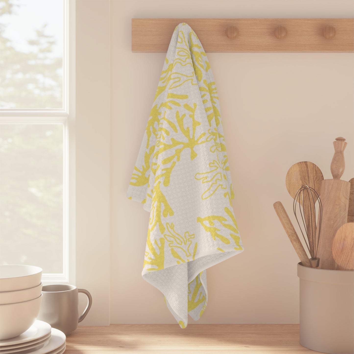 Microfiber kitchen towel featuring the original Global Village Kailua Coral Sunshine pattern in soft yellow and white, adding a bright island-inspired touch to any kitchen. The towel is hanging in a kitchen with kitchen utensils and plates.