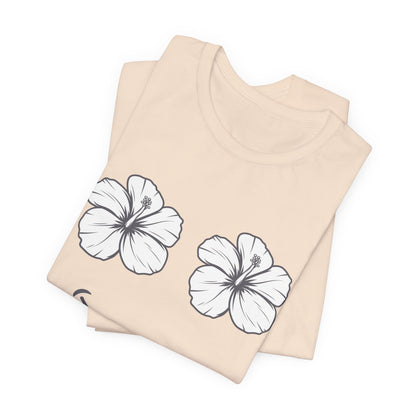 A folded light beige t-shirt with two white hibiscus flower graphics outlined in black, displayed on a clean white background.