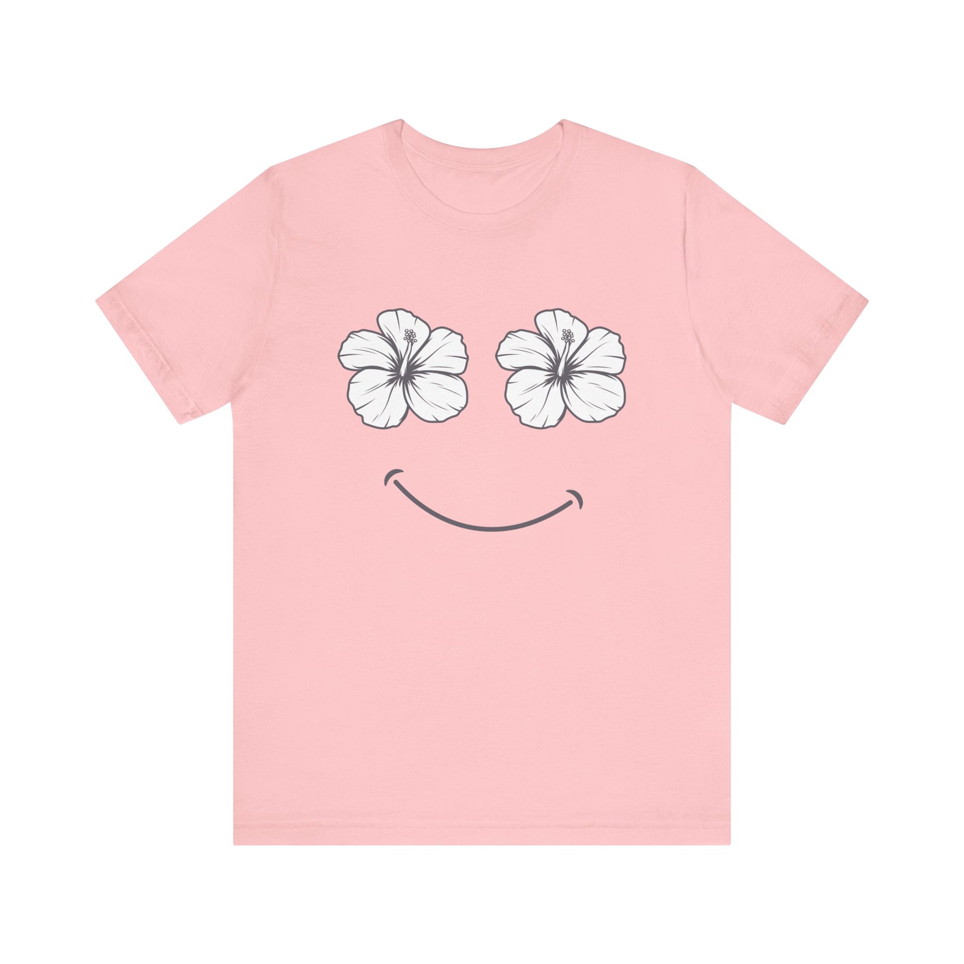 A light pink short-sleeve t-shirt with a graphic of two white hibiscus flowers forming eyes and a simple black smiley mouth on the front, displayed against a solid white background.
