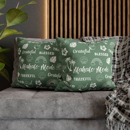 Two green throw pillows with white Hawaiian-themed text and illustrations, styled on a gray sofa with a wooden slat wall and a plaid throw blanket in the background.