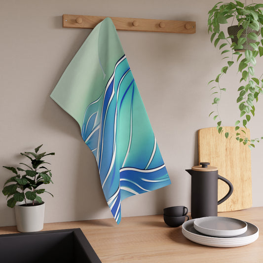 A kitchen towel with an abstract blue and green wave pattern hanging from a wooden peg on a beige wall above a kitchen counter with dishes and plants.