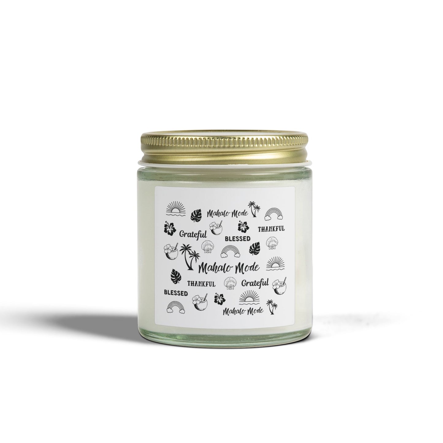 A glass jar candle with a gold metal lid and a white paper label featuring black tropical-themed illustrations and text like 'Mahalo Mode,' 'Grateful,' and 'Blessed,' shown on a clean white background.