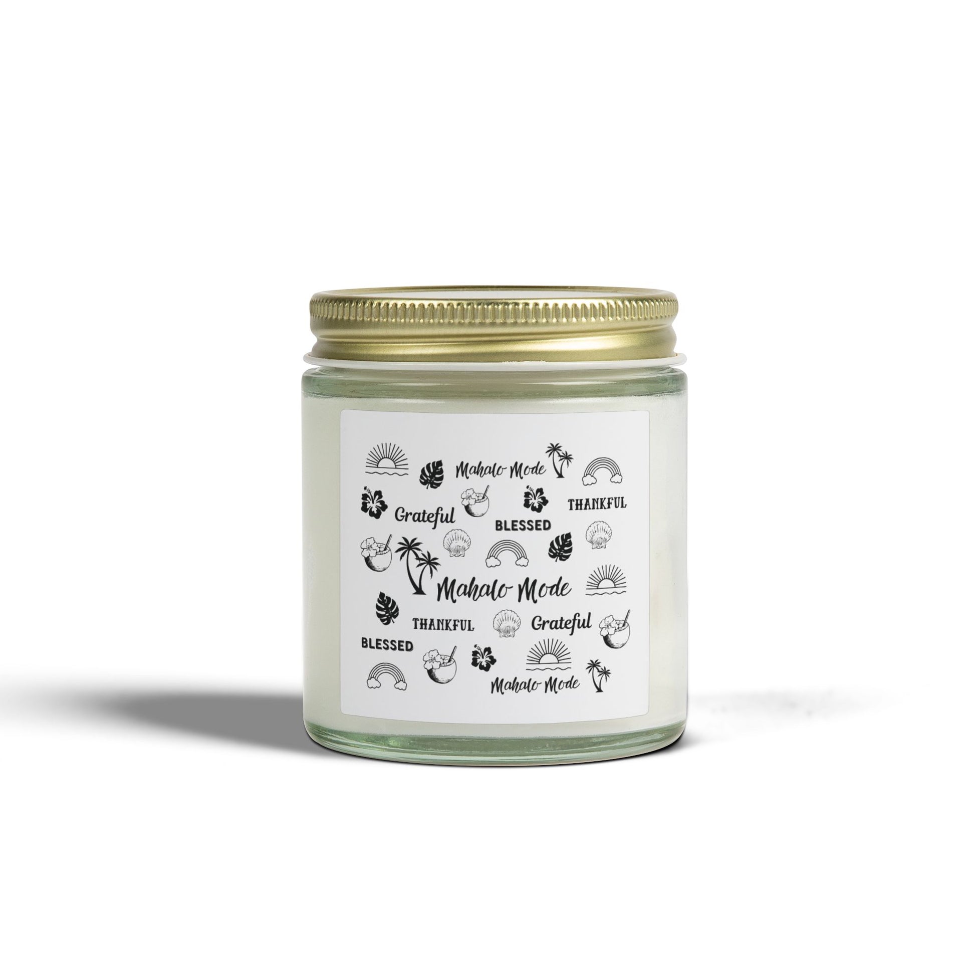 A glass jar candle with a gold metal lid and a white paper label featuring black tropical-themed illustrations and text like 'Mahalo Mode,' 'Grateful,' and 'Blessed,' shown on a clean white background.