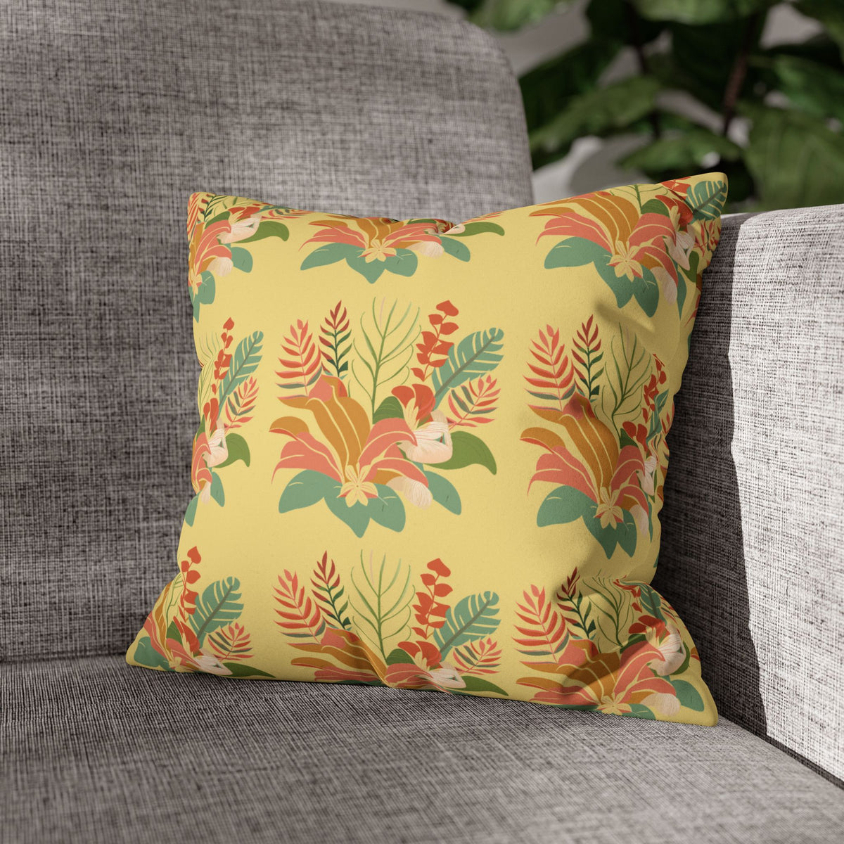A square throw pillow with a retro floral pattern in yellow, orange, green, and beige, resting on a gray textured fabric sofa.