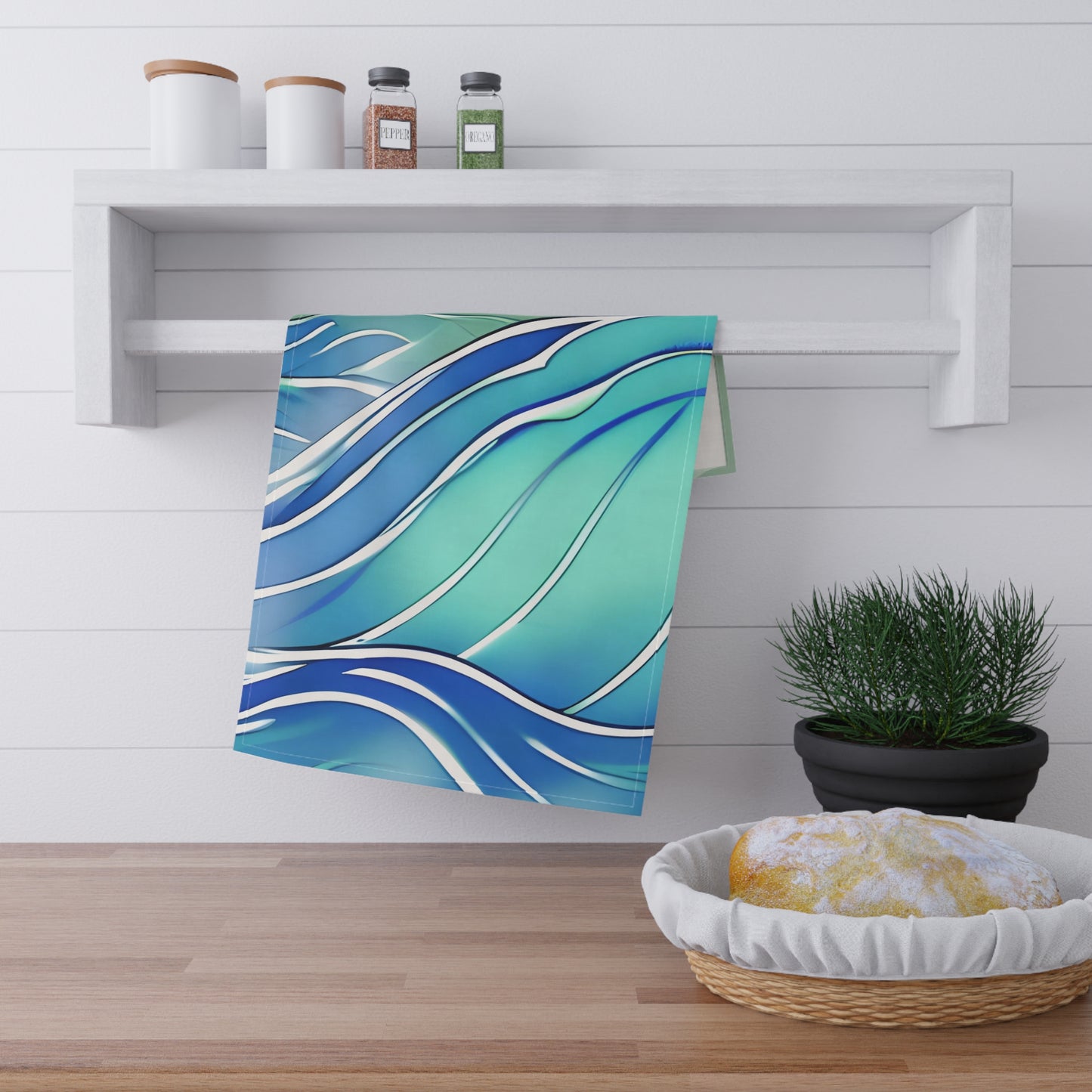 A kitchen towel with a blue and teal wavy pattern hanging from a white wall rack in a bright kitchen setting.