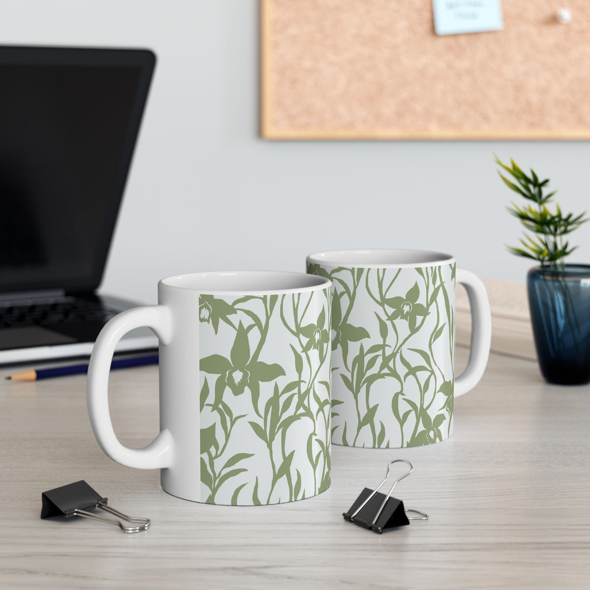 Two Orchid Sage coffee mugs with tropical orchid print by Global Village Kailua sitting on a desk with computer and binder clips.