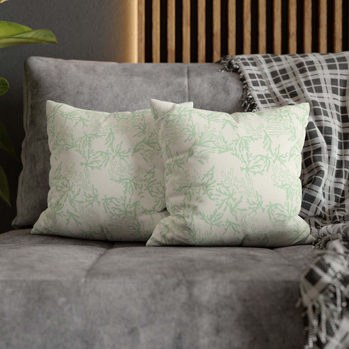 Two decorative pillows with sage coral branch patterns on a gray sofa.