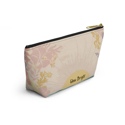 A rectangular zippered pouch with a beige background and a pink floral pattern, featuring a gold sunburst design and the words 'Glow Bright' on a gold label. The pouch has a black zipper and a gold zipper pull, shown on a clean white background.