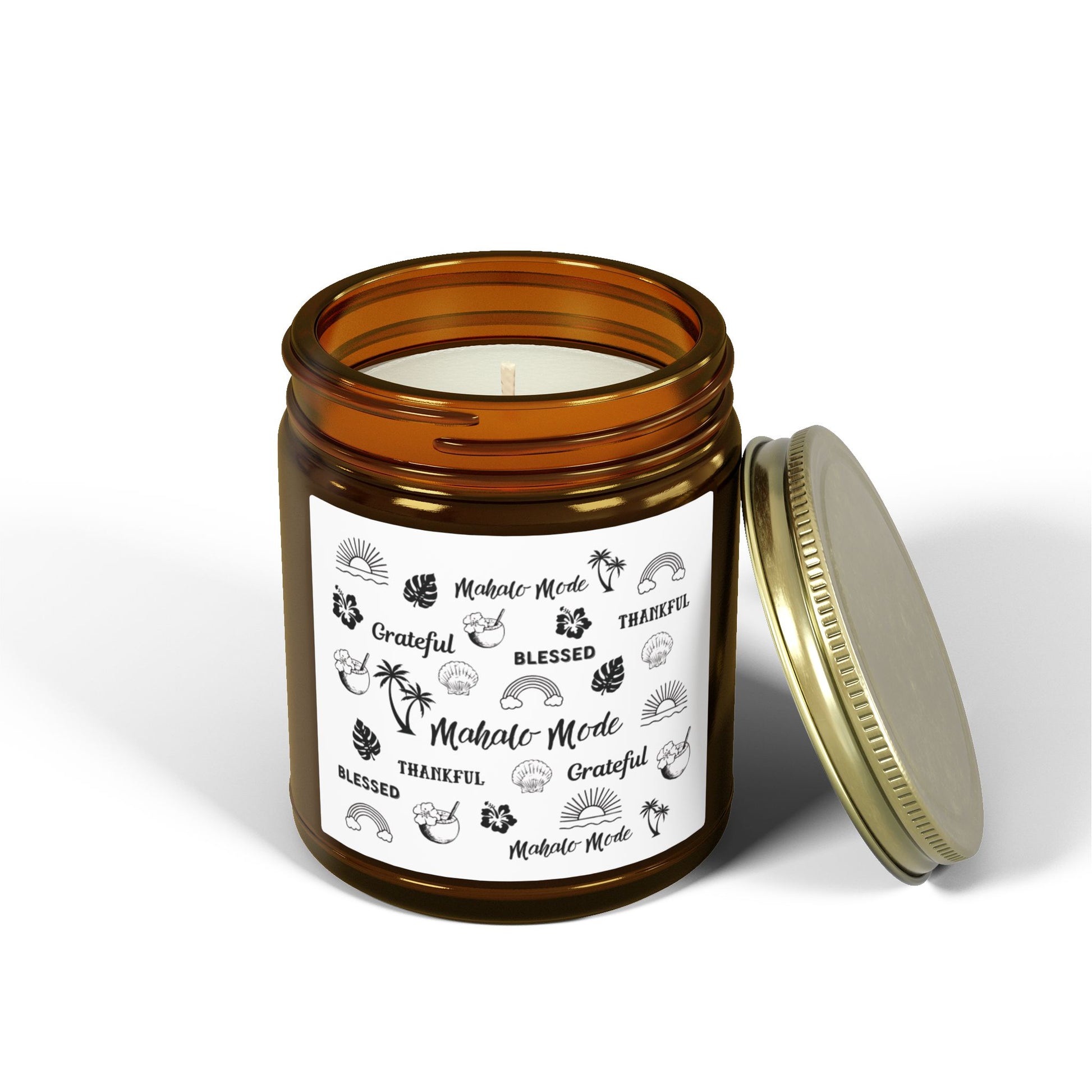 A dark amber glass jar candle with a gold metal screw-on lid and a white paper label featuring black hand-drawn style illustrations and the words 'Mahalo • Mode', 'Grateful', 'BLESSED', and 'THANKFUL'.