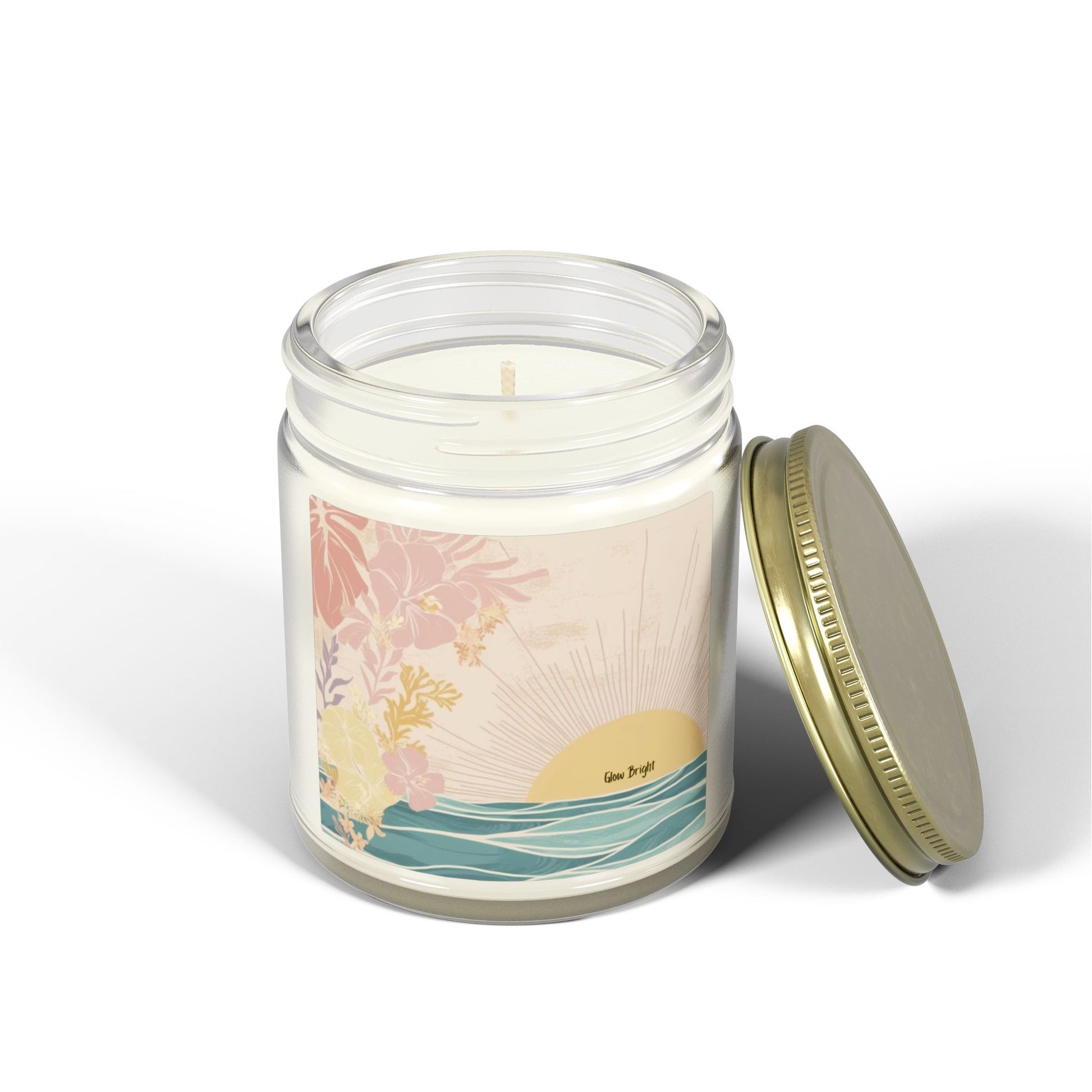 A glass jar candle with white wax and a gold metal lid, shown on a clean white background. The label features a pastel illustration of a sunset over the ocean with pink flowers.