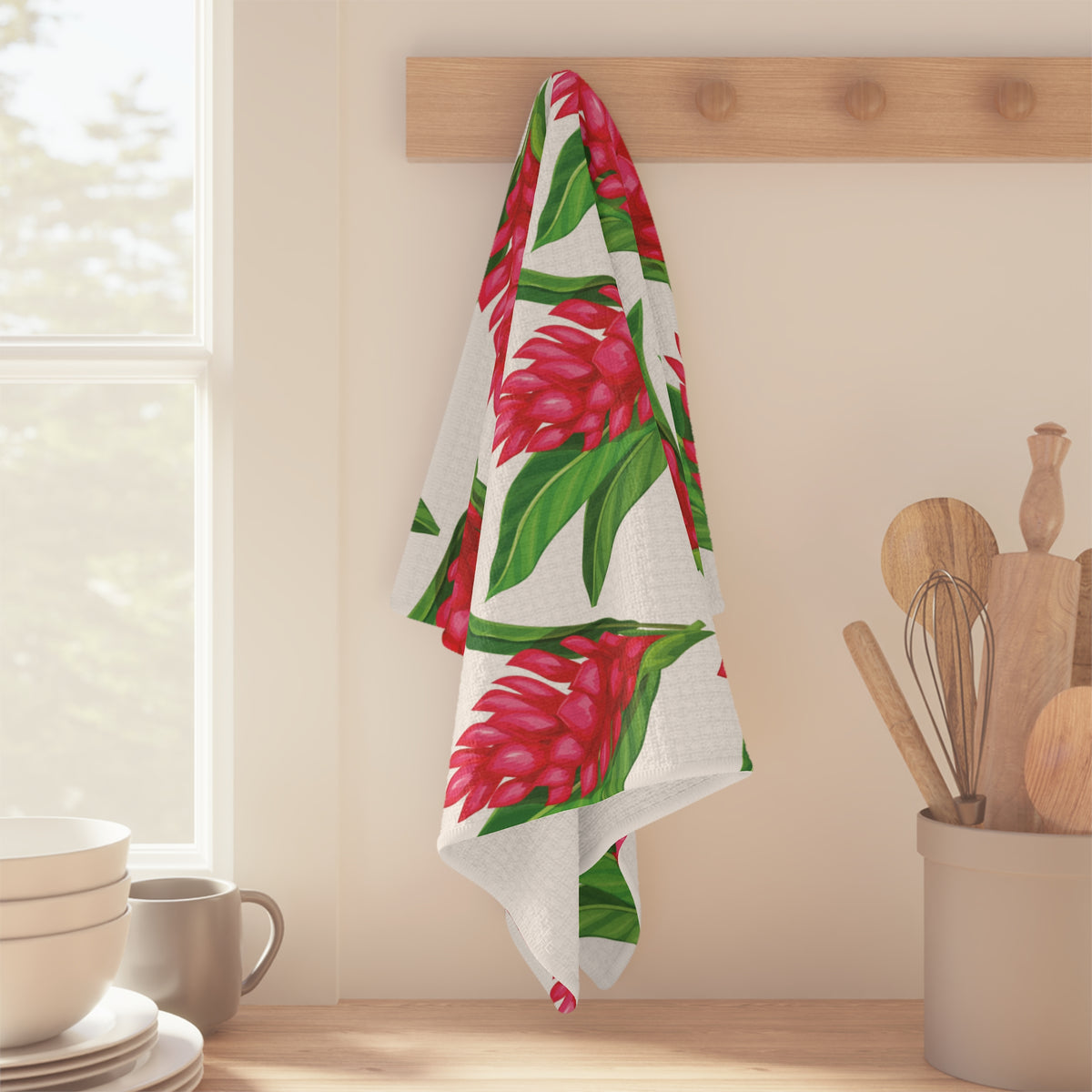 Red ginger Hawaiʻi kitchen towel with bright red tropical flowers and green leaves on white hanging off wood peg in a bright kitchen
