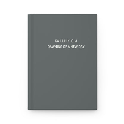 A dark gray hardcover notebook with white text on the front cover reading 'KA LÁ HIKI OLA DAWNING OF A NEW DAY', shown on a clean white background.