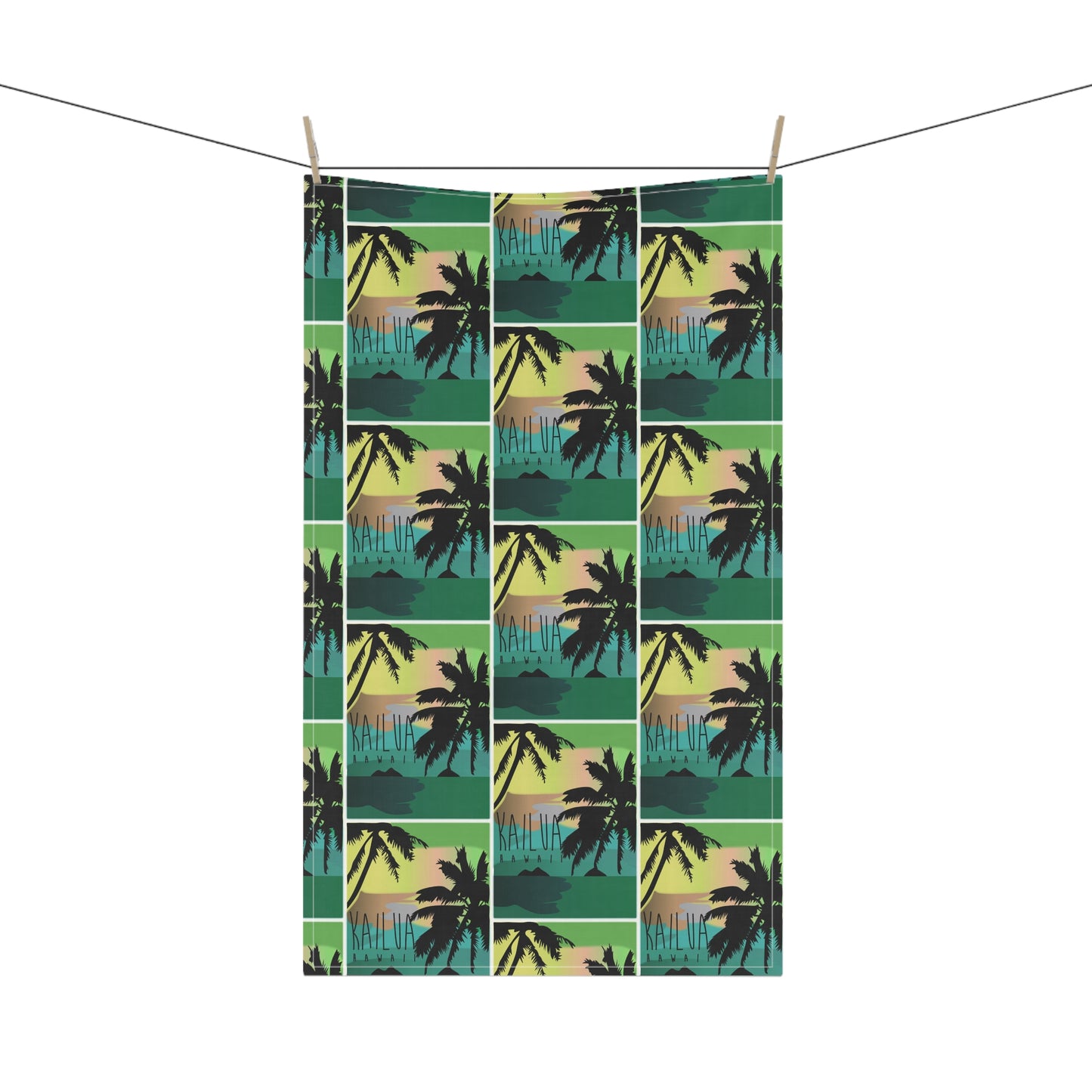 A tea towel with a repeating tropical sunset print 'KAILUA HAWAII' hangs from two wooden clothespins on a string against a plain white background.