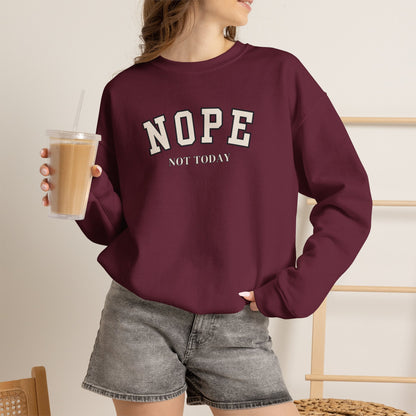 A woman wearing a maroon crewneck sweatshirt with black text reading 'NOPE NOT TODAY', paired with gray denim shorts, holding an iced coffee.