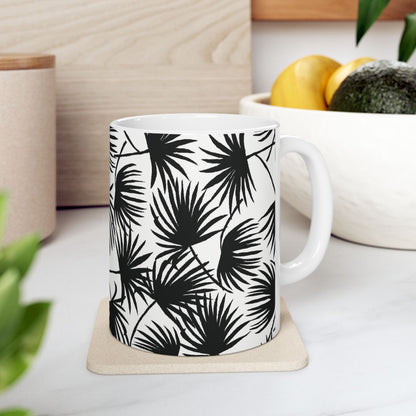 Palm Fan Black coffee mug with black and white tropical palm print by Global Village Kailua sitting on a coaster on a white kitchen counter with fruit bowl.