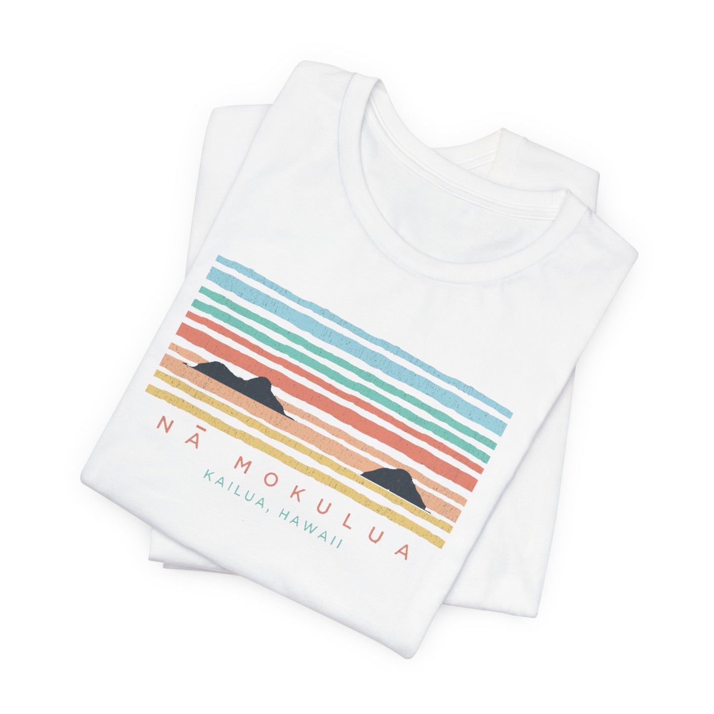 A folded white short-sleeve T-shirt on a clean white background, featuring a retro sunset-style graphic with horizontal pastel stripes and the text 'NÁ MOKULUA' and 'KAILUA, HAWAII'.