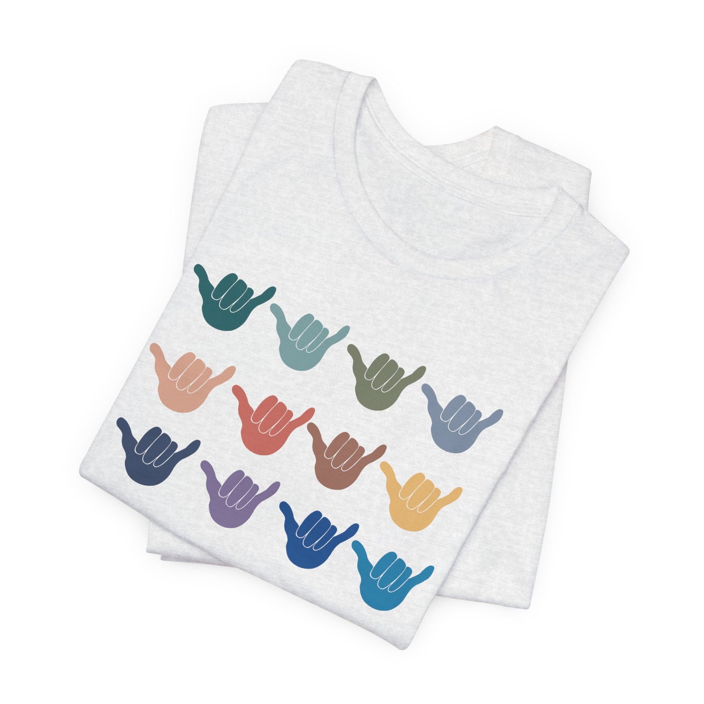 A folded white heather t-shirt featuring a grid of colorful shaka hand signs on the front, displayed on a clean white background.
