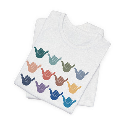 A folded white heather t-shirt featuring a grid of colorful shaka hand signs on the front, displayed on a clean white background.