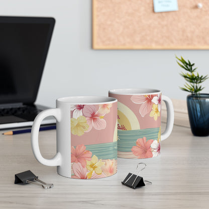Two white ceramic mugs with a pink tropical floral and sunset print, displayed on a light wood desk with office props like binder clips, a laptop, and a small plant.