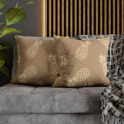 Two square throw pillows with a beige pineapple pattern on a taupe background, styled on a gray sofa with a black-and-white plaid throw blanket and a wooden slatted wall behind them.